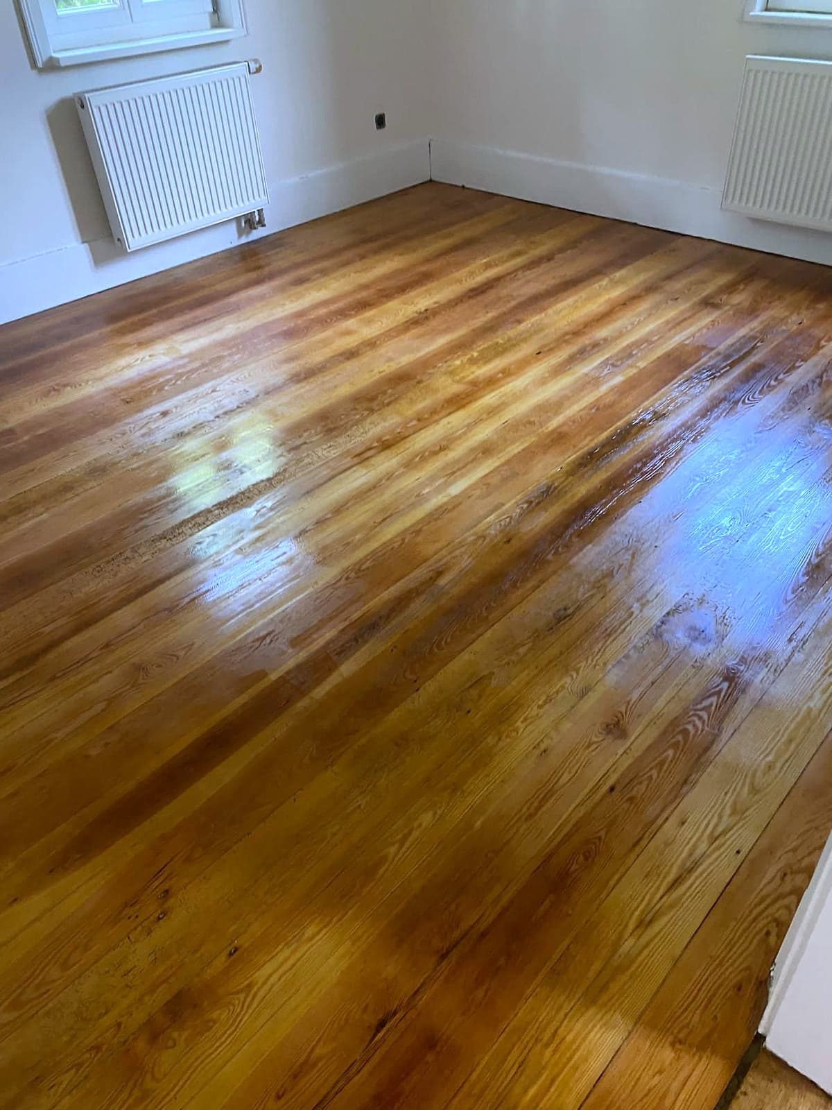 Aufgearbeiteter Dielenboden aus Nadelholz mit frischer Versiegelung, dahinter weiße Wand und Heizkörper