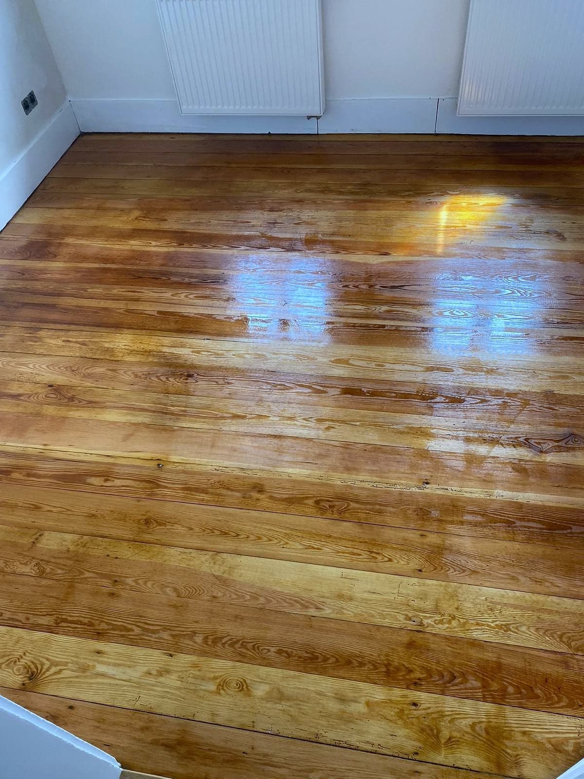 Aufgearbeiteter Dielenboden in einem leeren Zimmer, Tageslicht auf der Oberfläche